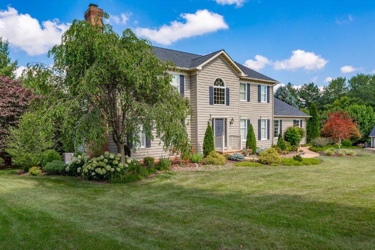 Large colonial home in Massanetta Springs, Virginia. The home features an immense green lawn, extensive landscaping, and a simple tan and blue exterior.