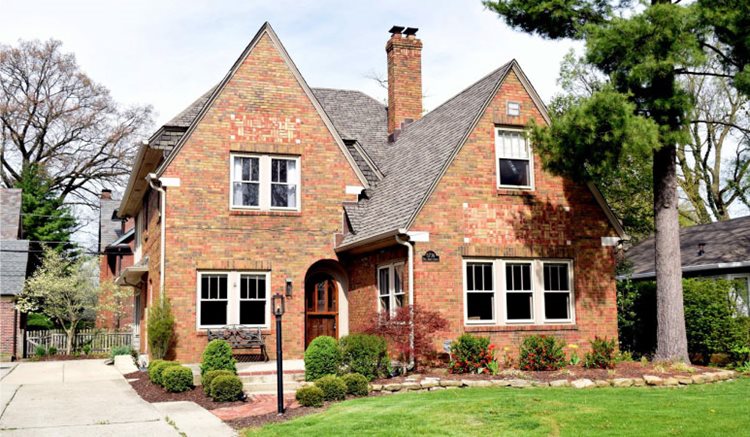 A two-story, red-brick, Tudor-style home in the Meridian-Kessler neighborhood of Indianapolis, featuring two front-facing gables, a central chimney, and an arched entryway.