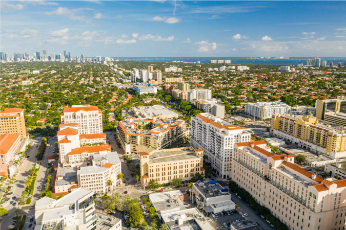 Aerial view of Downtown Coral Gables, Florida, with Miami and the Atlantic Ocean visible in the distance. 