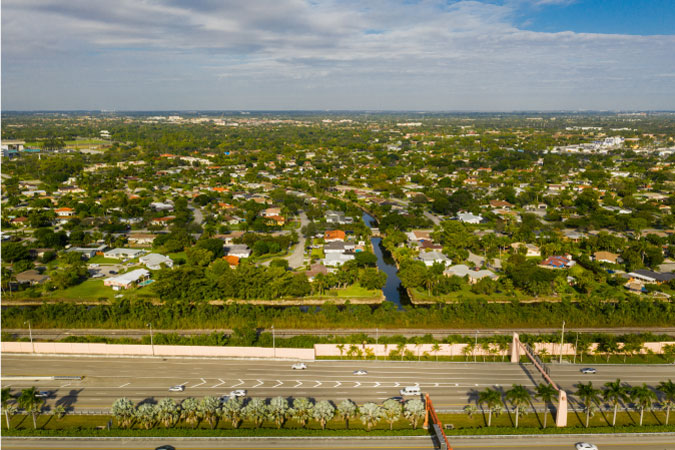Aerial view of residential neighborhoods in the Miami suburb of Kendall, Florida. There’s a large freeway crossing the foreground and a perpendicular canal running through the neighborhood.