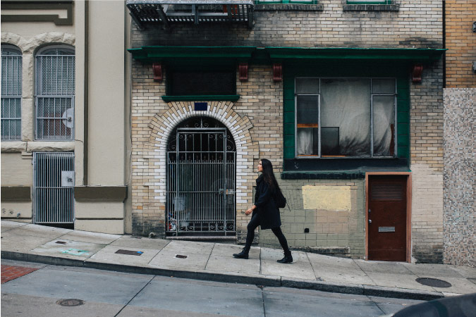 A woman dressed in black is walking up a steep sidewalk in San Francisco, California.