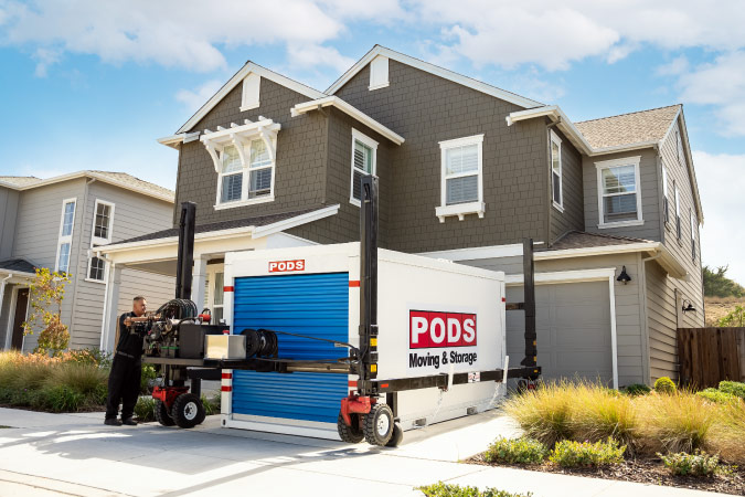 A PODS employee is using PODZILLA to deliver a PODS portable moving container to a residential driveway.