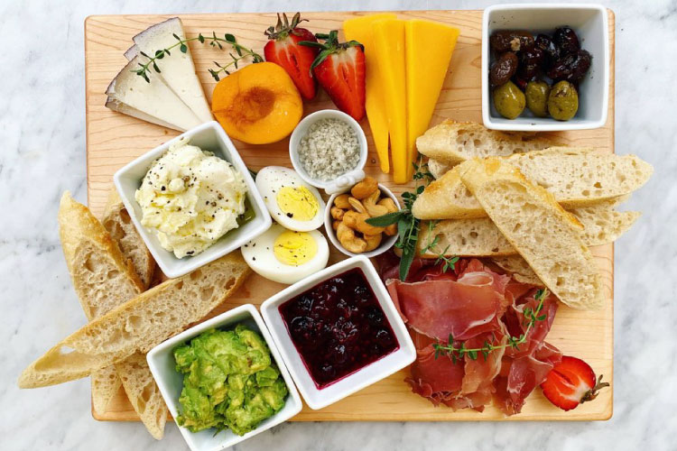 A brunch board from Arcadia Farms Cafe includes a variety of cheeses, olives, hard-boiled eggs, bread, prosciutto, smashed avocado, and more.