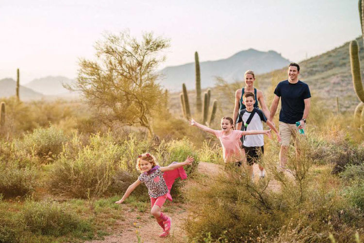 A family of five is taking a hike through the Sonoran Desert outside Scottsdale, Arizona. The parents are walking in the back as the three young kids run ahead.