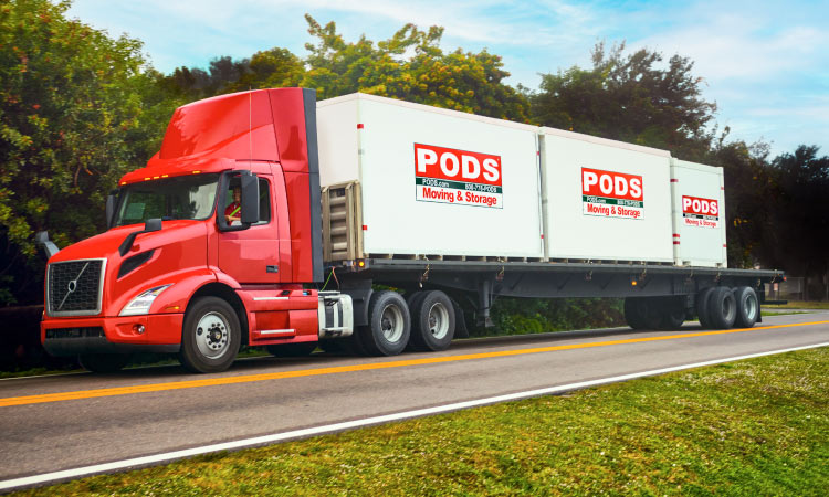 A PODS truck is transporting three PODS moving and storage containers along a tree-lined freeway.