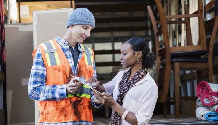 A moving company employee and a woman are signing a contract in front of a moving truck. 