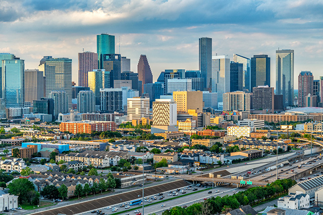 The Houston, Texas, skyline during the day. There are a mix of high-rise and low-rise buildings and two roads with traffic.