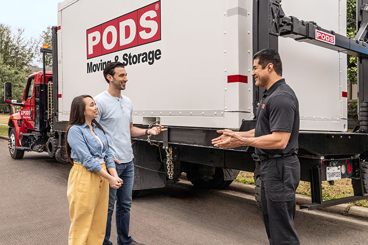 A young couple with a PODS truck driver. The truck is loaded with a container, thanks to PODZILLA. 