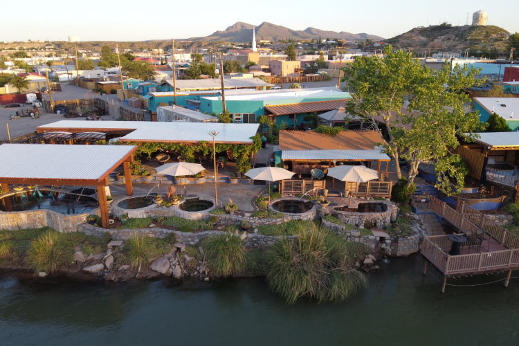 Aerial view of the town of Truth or Consequences in New Mexico. The Riverbend Hot Springs can be seen bordering the Rio Grande River in the foreground, and there are mountains in the distance. 