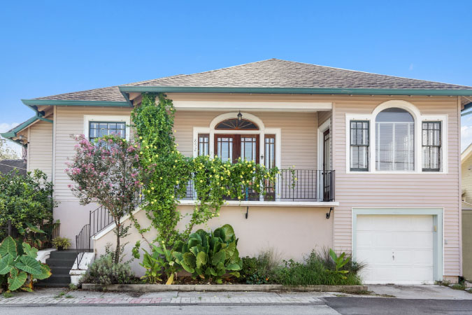 A two-story home in New Orleans’ Mid-City neighborhood, featuring lush plants in a narrow garden out front.