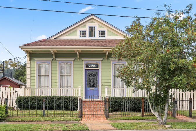 A quaint, one-story home in Bayou St. John, New Orleans, featuring a fenced-in yard and a blue door.