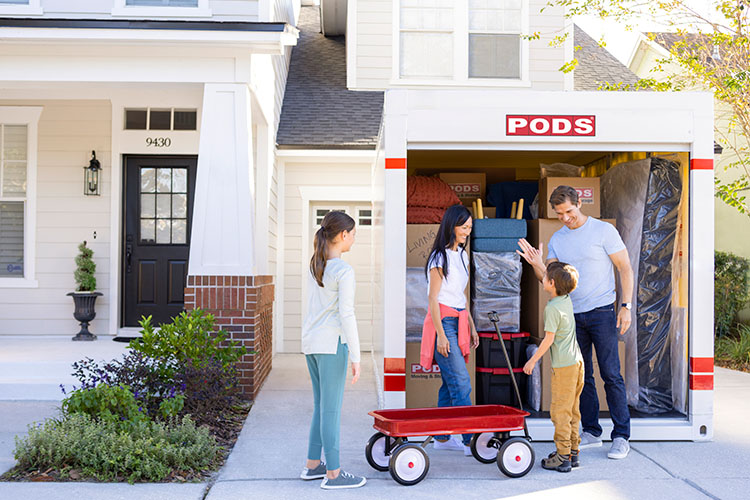 A family of four gathers in front of their open and full PODS container as they prepare for their move.