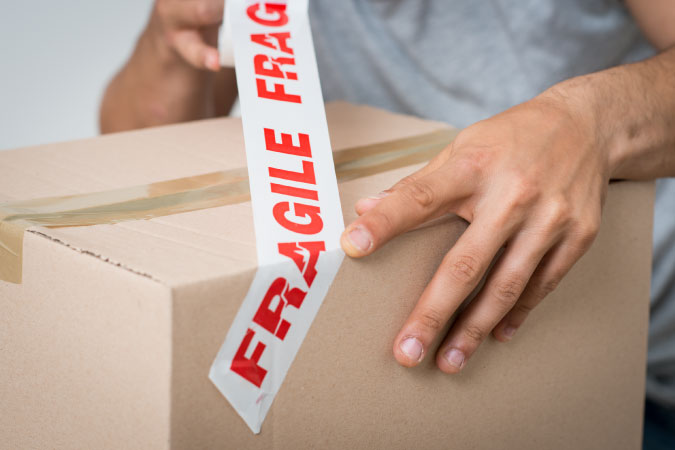  Close-up of a man using “FRAGILE” tape to label his box of glassware.