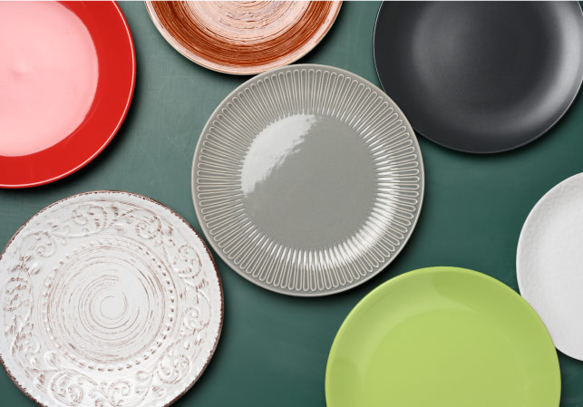 Seven unique dinner plates arranged on a flat green service, viewed from above. 