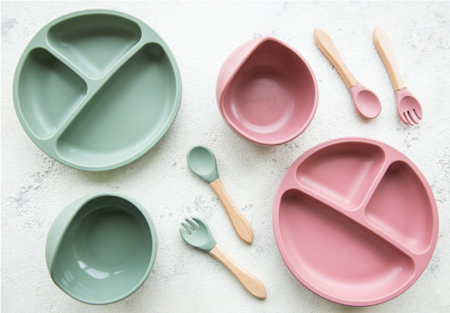  Pink and sage baby dishes arranged neatly on a white surface. 