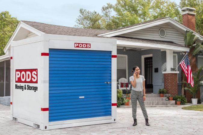 A soldier is standing in her driveway beside the PODS portable moving container that she rented for her DITY move.