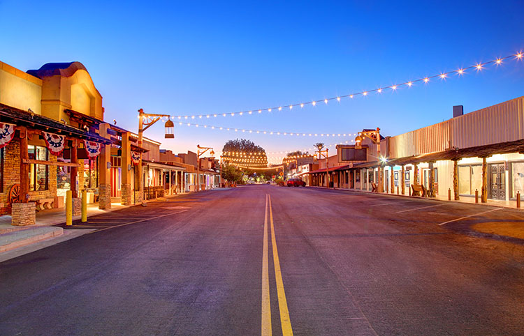 Old Town Scottsdale at dusk with warm streetlights pouring onto the road. Low buildings and saloon-style doors give the area an old-west fool.