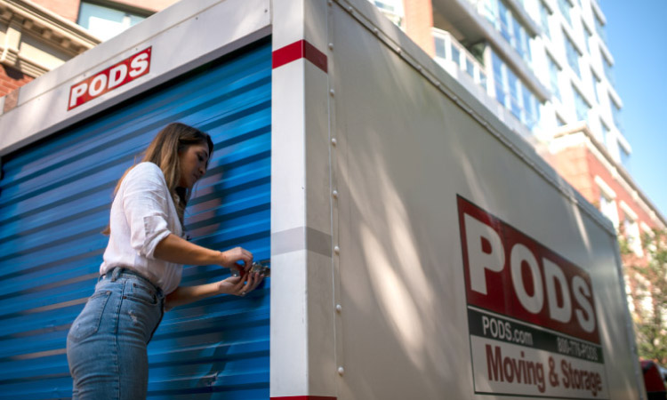 A young woman is unlocking the blue door of her PODS portable moving and storage container.