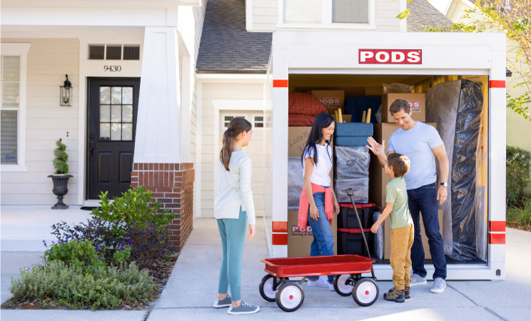 A family of four is standing by the front of their PODS portable moving container. 