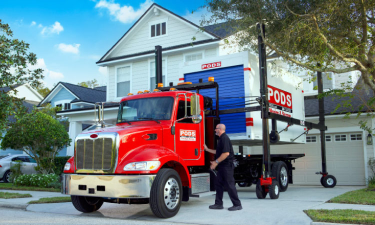 A PODS driver is reaching to open the door of his truck’s cab. It is parked in a residential driveway.