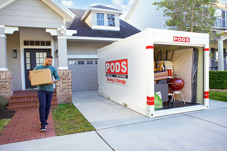 A man loading a box labeled “bedroom” into a PODS container