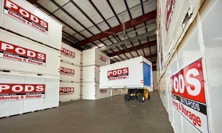 A forklift driver is moving a PODS portable storage container through a large warehouse.