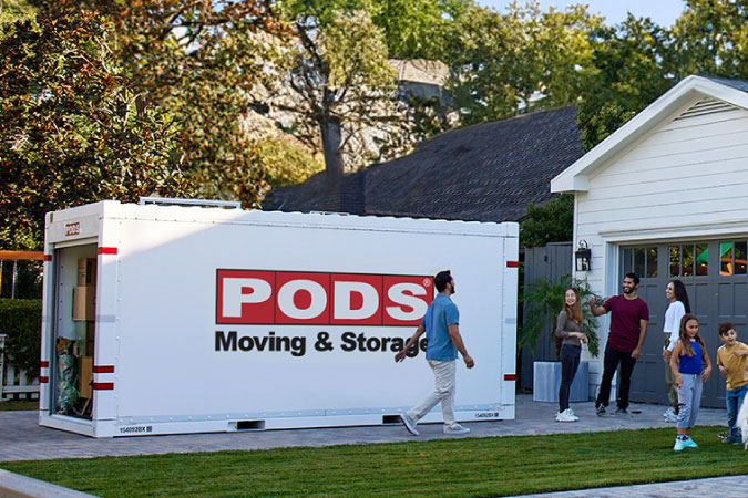 A family is hanging out in the driveway beside a loaded PODS portable moving container.