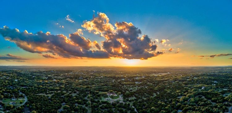 An aerial view of Dripping Springs, Texas, as the sun sets behind fluffy clouds.