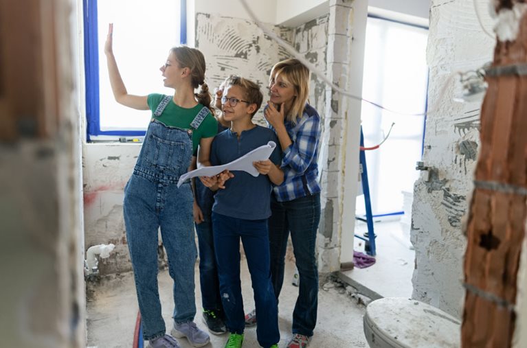 A mother and her three children are standing in a bathroom that is being remodeled while holding the plans for the remodel