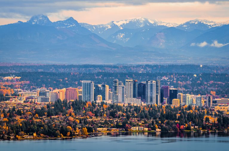 Distant view of the waterfront city of Bellevue, Washington, with the forests and snow-capped mountains behind it.