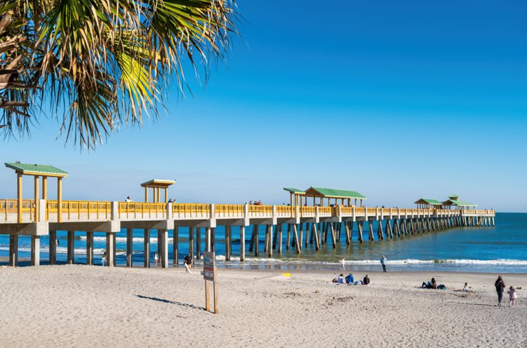 Locals enjoy a beach day by the pier on Folly Beach in South Carolina on a sunny summer day.