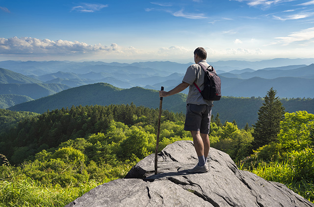 A hiker standing on the ridge of a cliff overlooking the Carolina mountains.