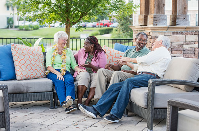A group of friends sit on an L-shaped couch, enjoying each others’ company in their retirement.