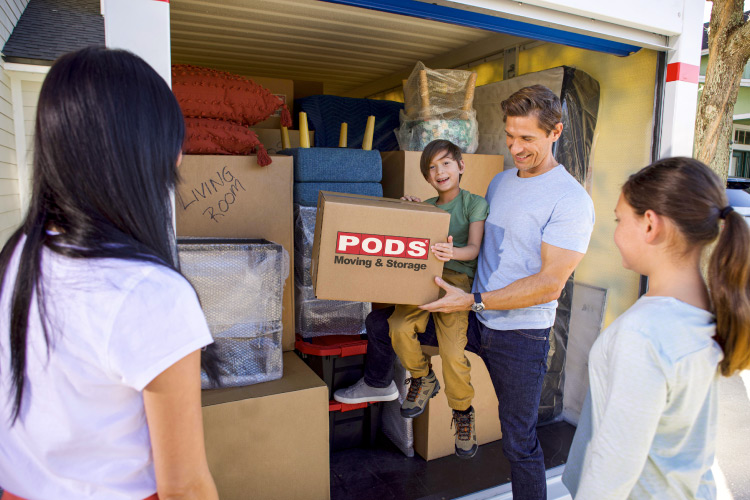 A family of four is standing by their PODS portable moving container which has been efficiently loaded with moving boxes and furniture.