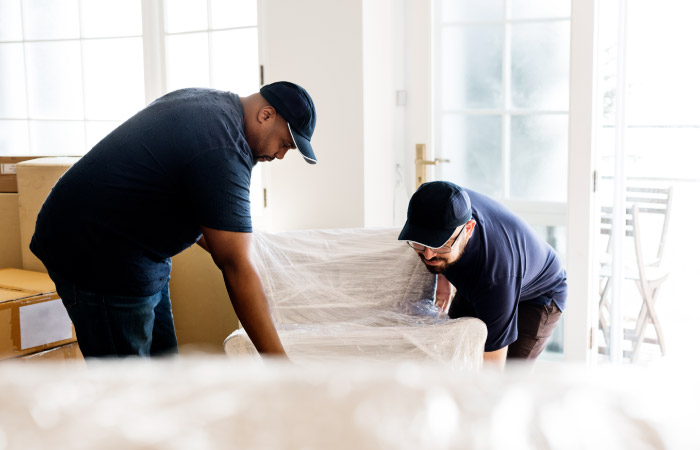 Professional movers wrap a chair in a protective plastic film during a move. 