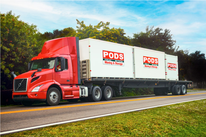 A large truck is transporting three PODS portable moving and storage containers along a freeway