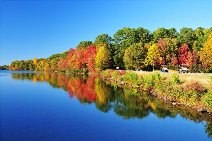 Golf carts travel beside a body of water through fall foliage in Peachtree City, Georgia