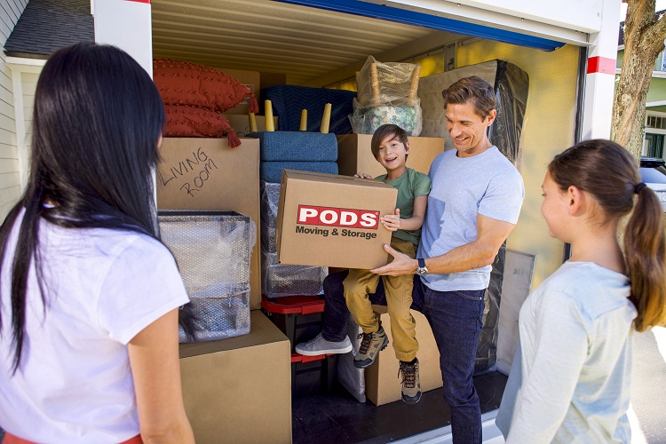 A father holds his son as he loads a PODS-branded moving box into a full PODS container