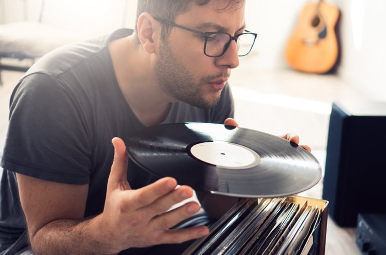 A man is holding a vinyl record and lightly blowing the dust off its surface before storing it away securely.