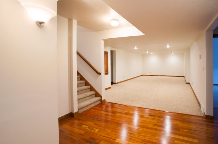 View of a finished basement with carpeted stairs, white walls, and a mix of carpeted and hardwood flooring.