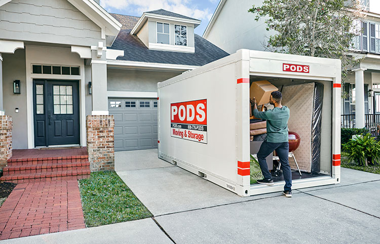 A man is loading his PODS container in his driveway.