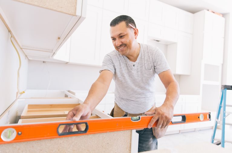 A man is checking if his cabinets are level during a DIY kitchen remodel.