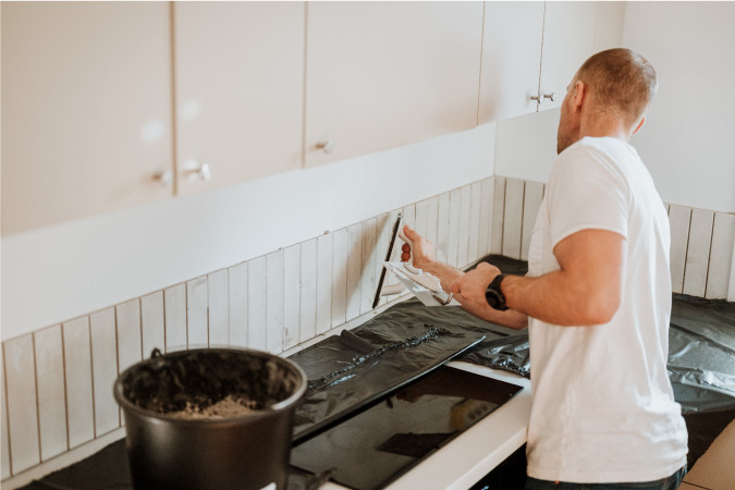  A man is installing vertical tiles as a backsplash during his DIY kitchen remodel