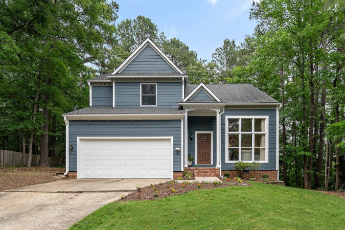 A simple, two-story home with a covered entry and forested backyard in Durham’s Hope Valley Farms neighborhood.