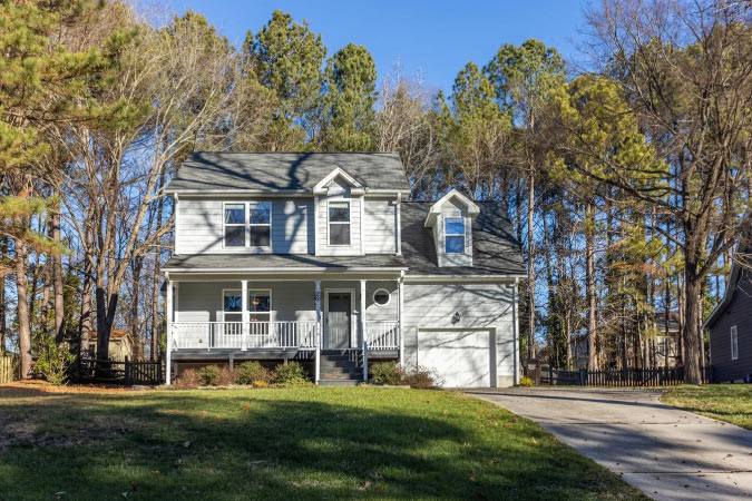 View from below of a lovely two-story home perched atop a hill and surrounded by pine trees in Durham’s Woodcroft neighborhood.