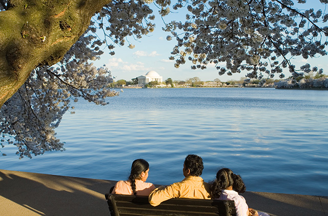 A family sits on a bench by a lake with the Jefferson Memorial in the distance