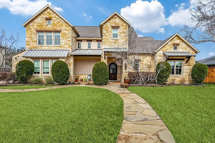 A home in the Russwood Acres neighborhood in Dallas, Texas. There is a stone path that leads up to the home with green grass on either side. There are hedges lining the home.