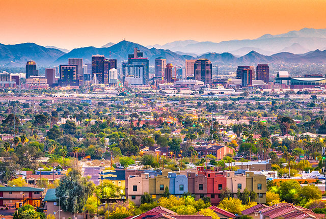 The skyline of Phoenix, AZ during the day. The sky is orange. There are colorful buildings in the foreground with the city skyline in the background. 