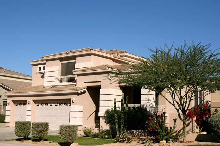 A beige two story home in Ahwatukee Foothills. There are two garages and bushes and trees in the yard. 