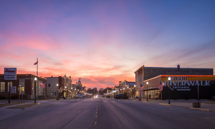 A street-level view of downtown Council Grove, Kansas, at sunset. On the right is the entrance to the Neosho Riverwalk Trail. 